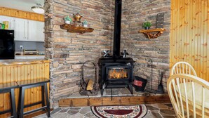 Una chimenea de piedra con un conducto negro, estantes de madera con adornos, un banco de madera rústico y una silla de madera.