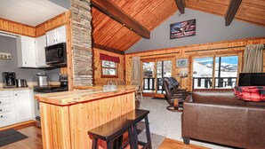 Interior acogedor de una cabaña con cocina de madera, comedor y sala de estar con vistas a las montañas.