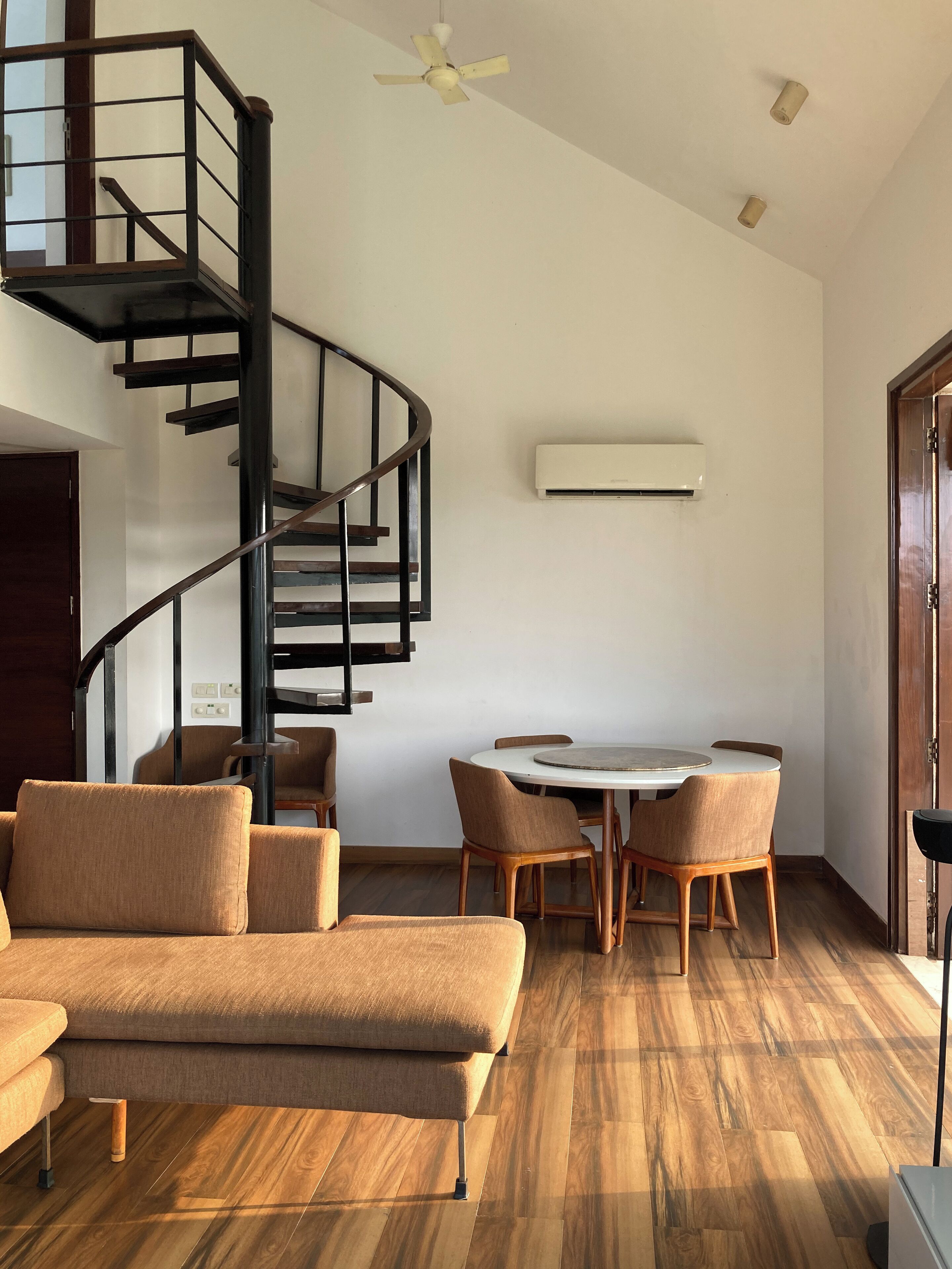 Ein modernes Wohnzimmer mit Wendeltreppe, einem Essbereich mit Holzkästen und einem Deckenventilator.