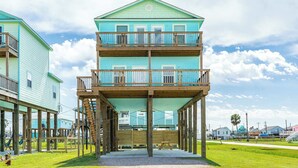 A multi-story building with a balcony on the second floor, wooden deck, and a grassy area in front. - Spacious 3 Bedroom Surfside Home Near The Jetties (Surfside Beach)