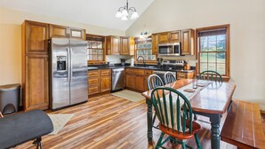 A kitchen with wooden cabinets, stainless steel appliances, and a dining area with a table and chairs. - Come stay! Sam's Cabin is a genuine mountain treasure. (Canaan Valley)