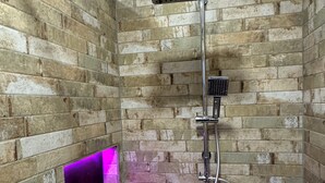Une douche équipée d’un pommeau de douche en métal et d’un pommeau de douche portatif, le tout installé devant un mur de briques.