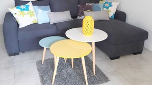 Un salón moderno con un sofá seccional gris, dos mesitas redondas y un farol amarillo.