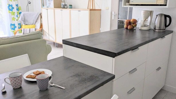 Una cocina compacta con encimera oscura, armarios blancos y una cafetera.