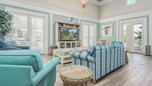 A spacious living room with a large television, comfortable seating, and a decorative ceiling light. - Gorgeous Sunsets, 2 minutes to the beach - Cinnamon Beach 1032! (Palm Coast)