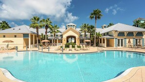 A swimming pool surrounded by palm trees and lounge chairs, with a building featuring a central archway and multiple balconies. - Gorgeous Sunsets, 2 minutes to the beach - Cinnamon Beach 1032! (Palm Coast)