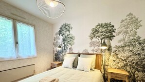 A bedroom with a large bed, a nightstand, a lamp, and a wall mural. - La Baraque de Papi - Spacious detached house - Private garden (Marck)