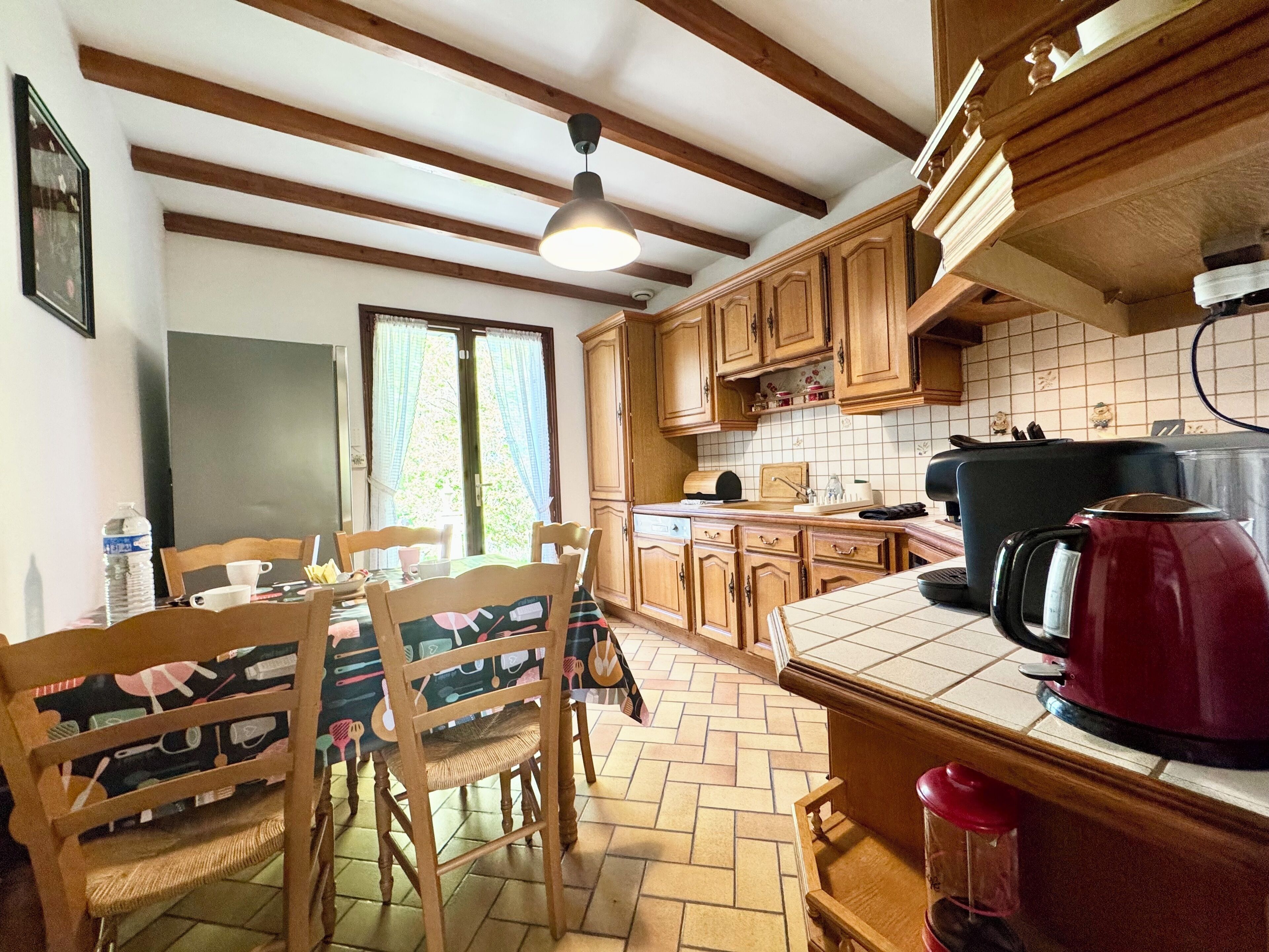 Een keuken met houten kastjes, een betegelde spatwand en een eethoek met een tafel en stoelen.