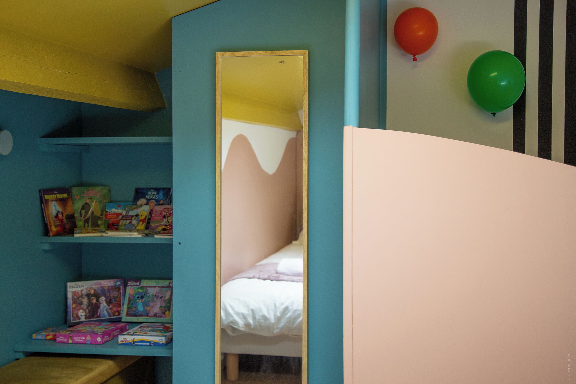 Une chambre à coucher avec un lit, une étagère remplie de jouets et un miroir.