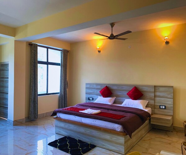 Une chambre d’hôtel avec un grand lit, deux tables de chevet, un ventilateur de plafond et une fenêtre avec des rideaux.