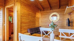 Interior em madeira com mesa de jantar, cadeiras brancas, sofá e espelho na parede.