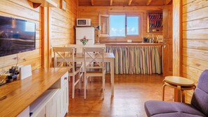 Een gezellig houten interieur met een eethoek met stoelen, een kleine keuken met een koelkast, en een televisie op een houten tafel.