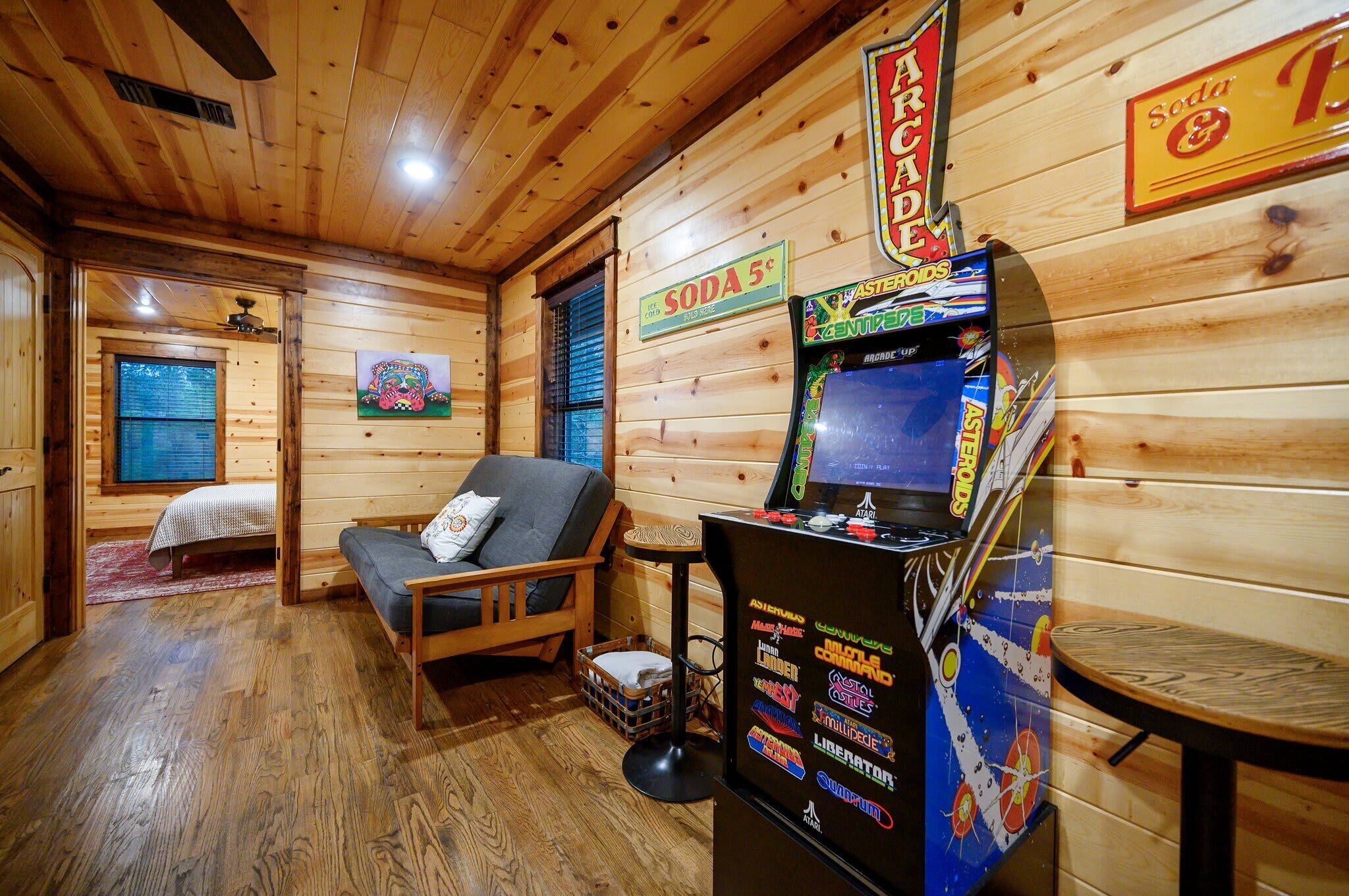 Ein Holzblockhaus-Interieur mit einem Bett, einer Couch, einer Bar mit Spielautomaten und einem Getränkeschild.