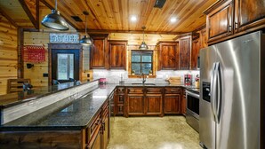 A wooden cabin interior with a kitchen featuring a stainless steel refrigerator, wooden cabinets, and a granite countertop. - Sugar Mama - great location, sleeps 10, hammocks (Broken Bow)