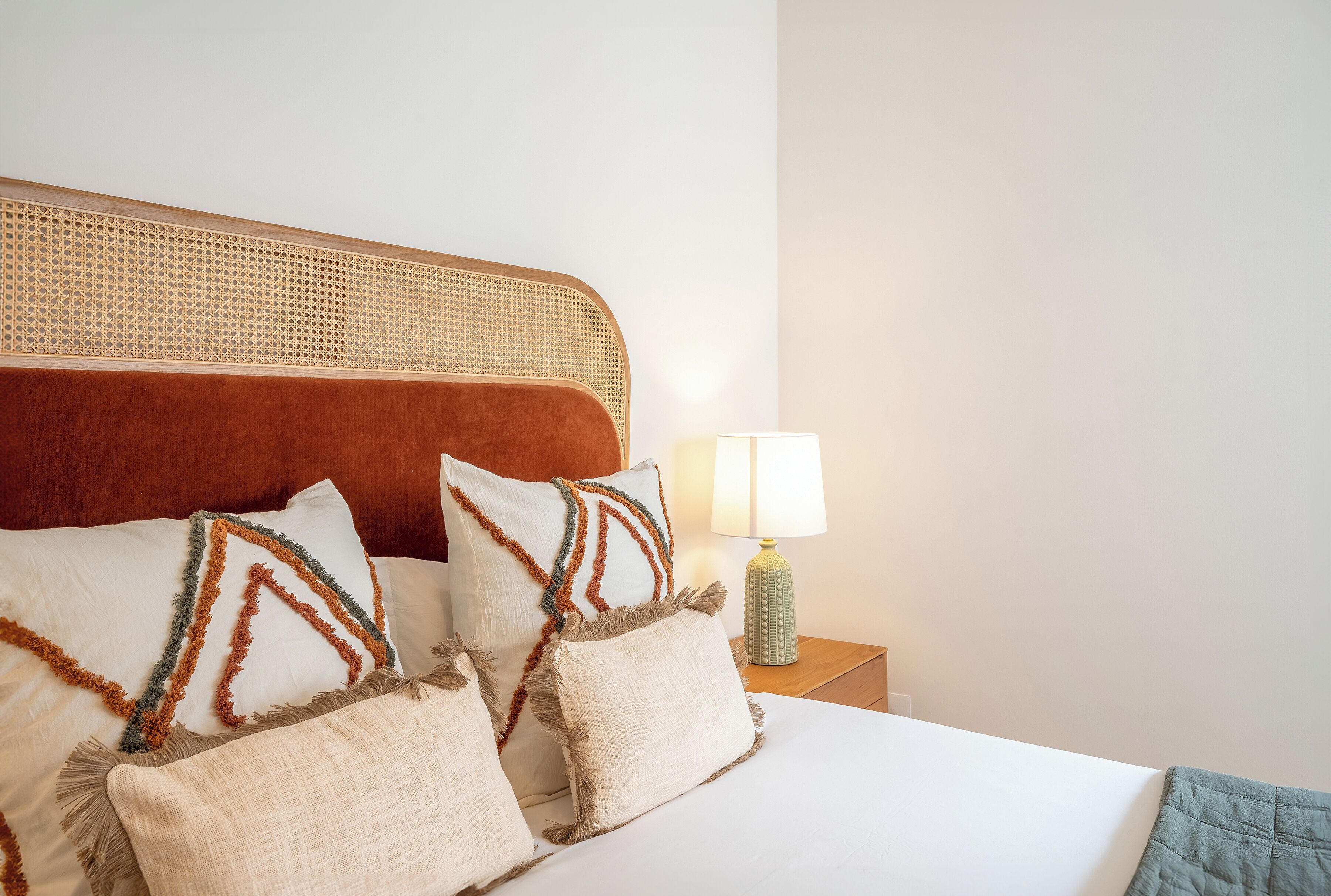 Een net opgemaakt bed met decoratieve kussens en een rieten hoofdbord.