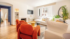 Una sala de estar moderna con un sofá blanco, sillones naranja, una mesa de centro y un televisor en la pared.