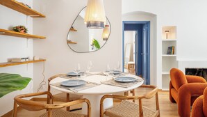 Comedor con una mesa redonda dispuesta para seis personas, rodeada de sillas de mimbre. Un espejo grande cuelga en la pared, reflejando la habitación.