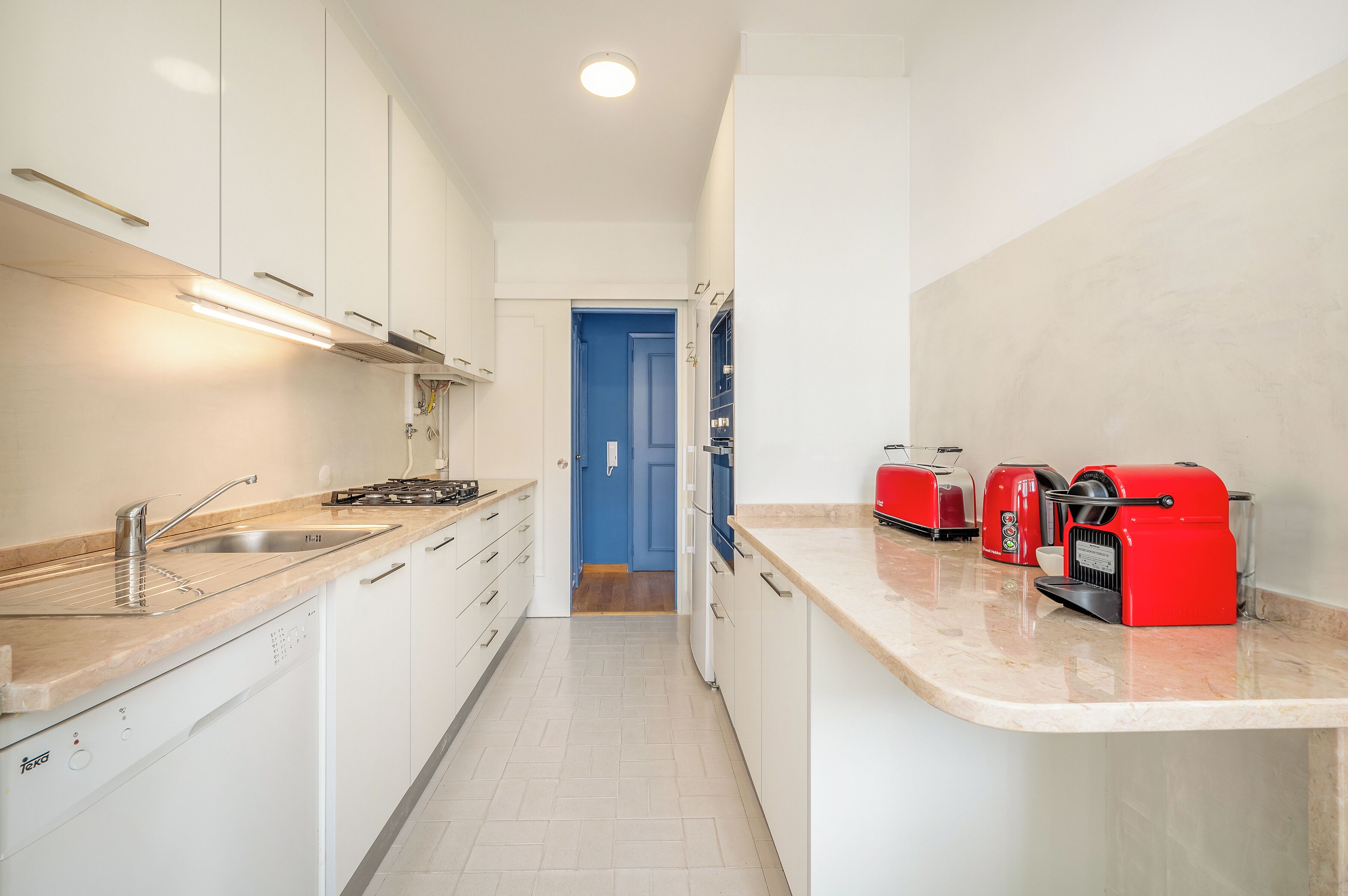 A modern kitchen with white cabinets, a stainless steel sink, a dishwasher, and a red coffee machine.