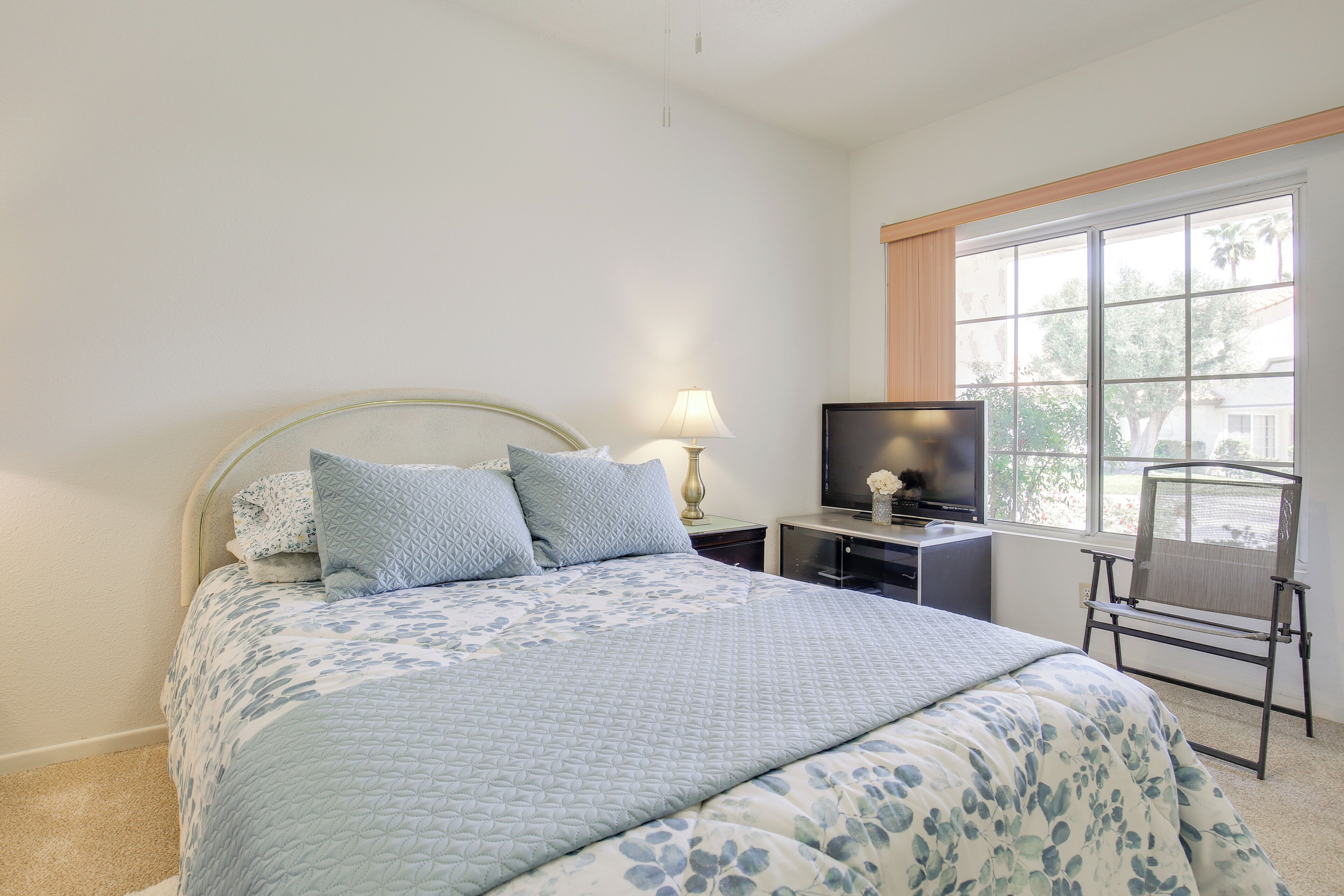 Une chambre à coucher avec un lit, une télévision, une lampe et une fenêtre donnant sur des palmiers.