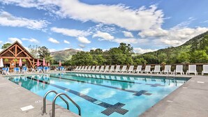 A swimming pool with lounge chairs and umbrellas, surrounded by mountains and a wooden building.