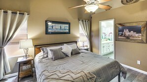 Une chambre à coucher comprenant un lit, une table de chevet, un ventilateur de plafond et deux tableaux accrochés au mur.