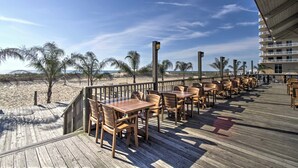 Une terrasse en bois avec des tables et des chaises donnant sur une plage.