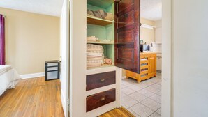 Quarto com piso de madeira, uma cama, um guarda-roupa com prateleiras e um espaço com cozinha.