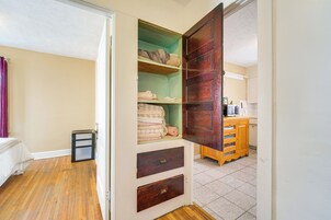 Una habitación con piso de madera, una cama, un armario con estantes y una zona de cocina.