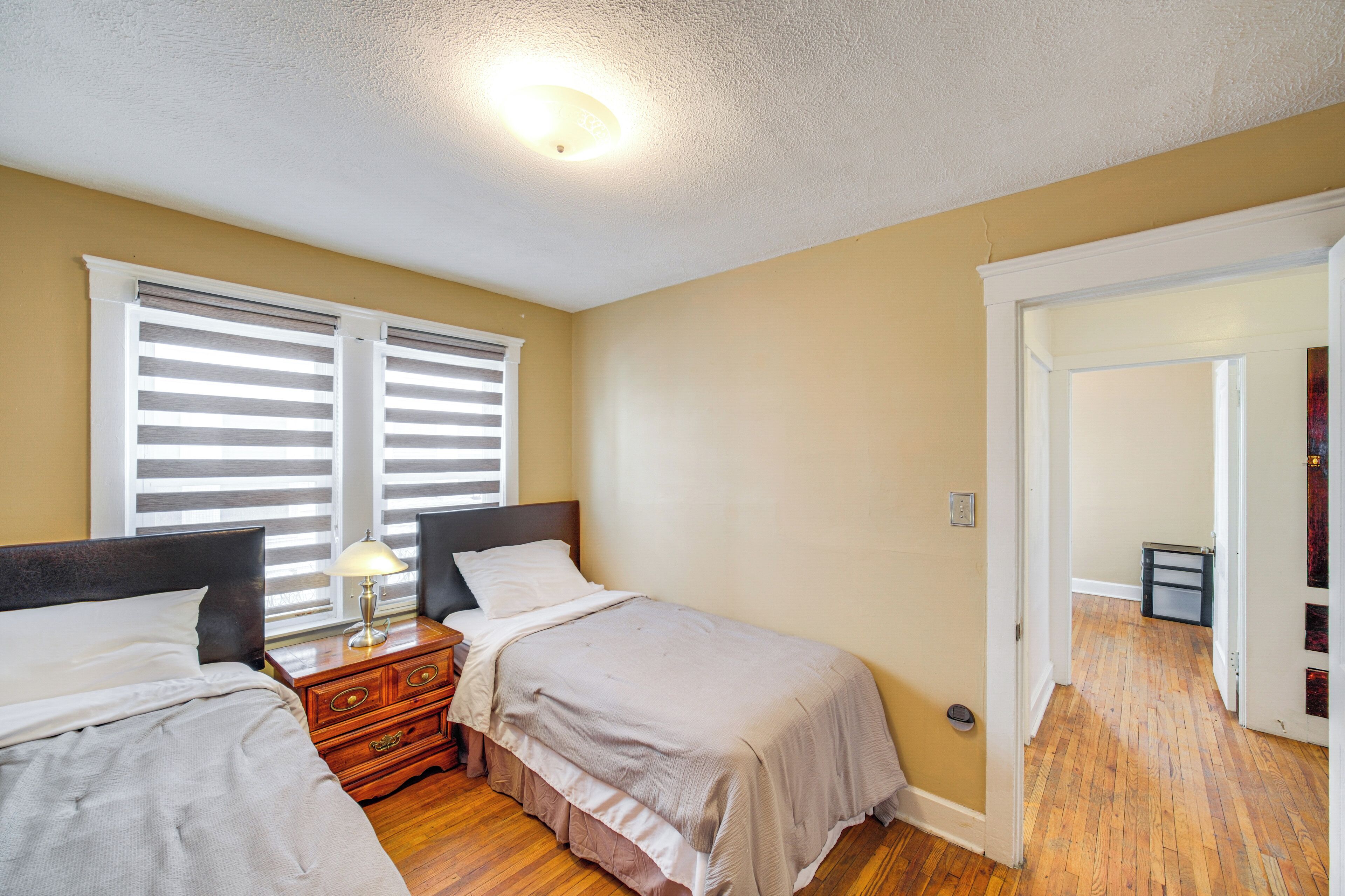 A bedroom with two beds, wooden flooring, and a ceiling light fixture.