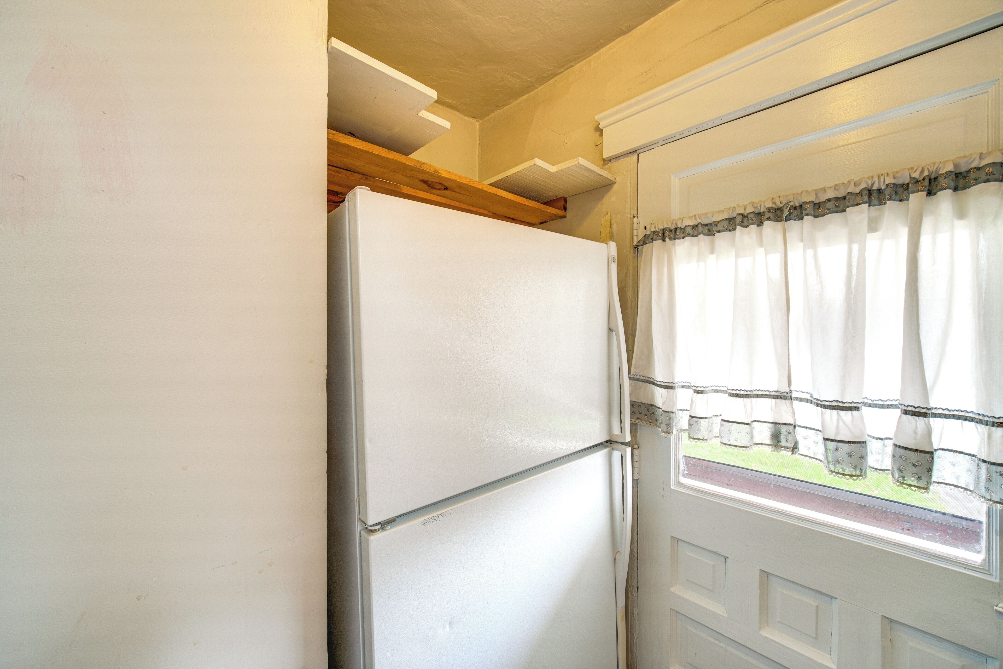 Un refrigerador blanco en una cocina con ventana y una puerta con cortina.