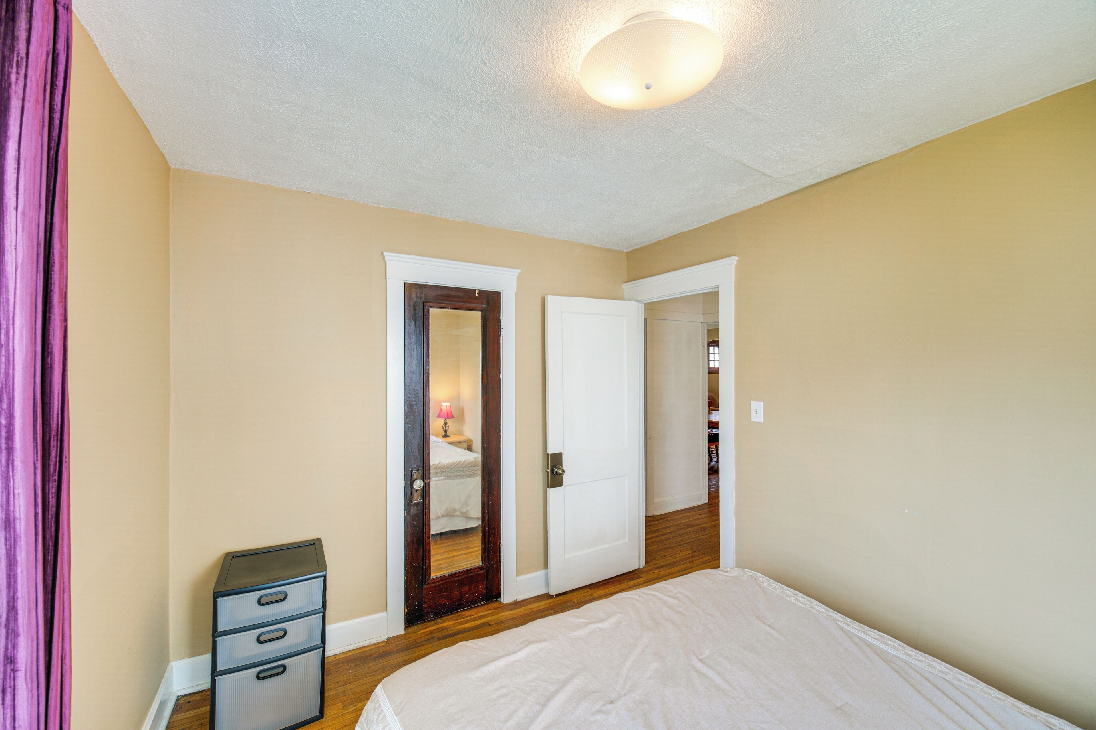 Ein Schlafzimmer mit einem Bett, einem Schminktisch und zwei Türen zu weiteren Räumen.