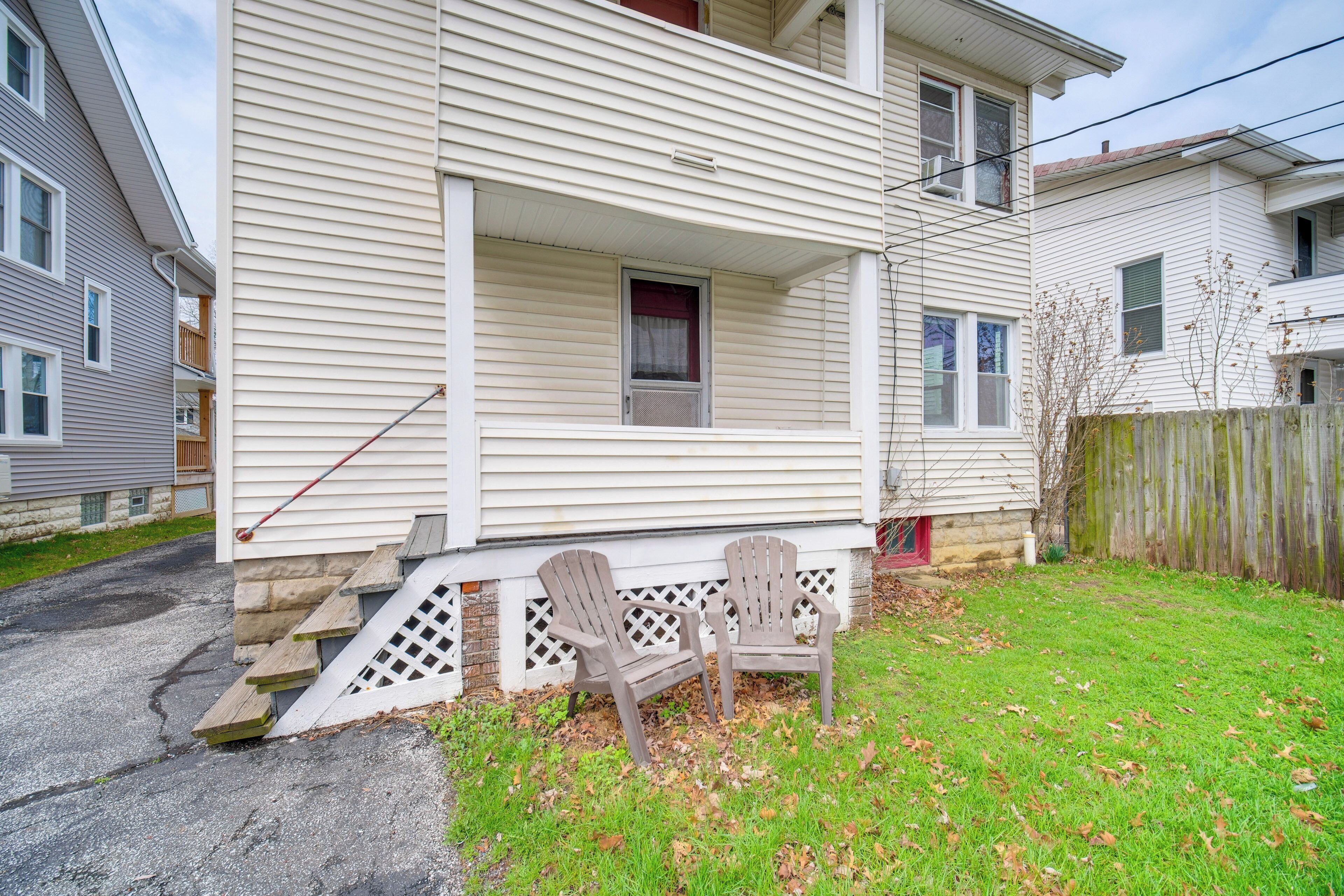 A two-story house with a front porch, a wooden fence, and two Adirondack chairs.