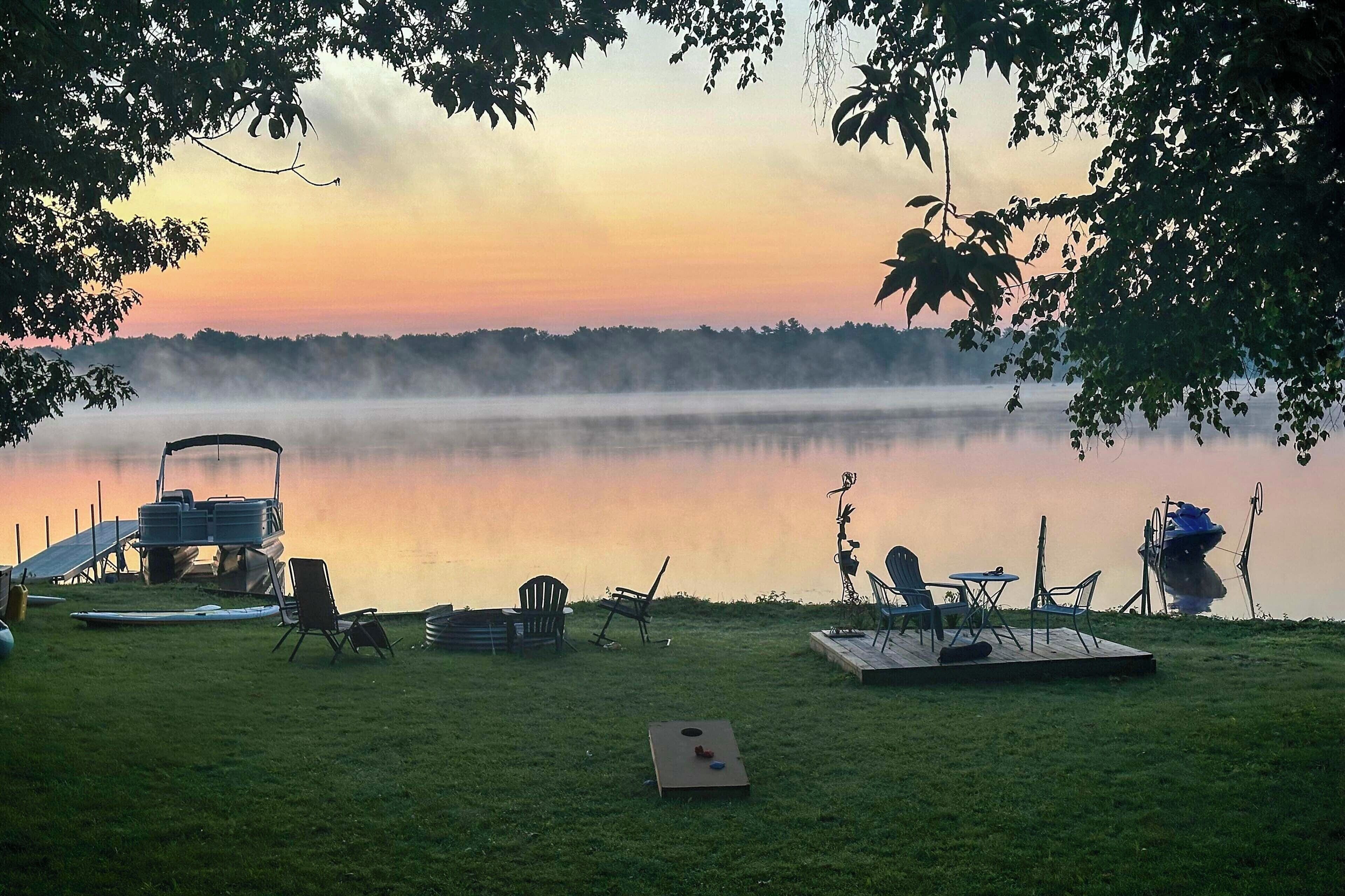 Ein Campingplatz am Seeufer mit einem Boot, Stühlen und einem Stand-Up-Paddleboard.