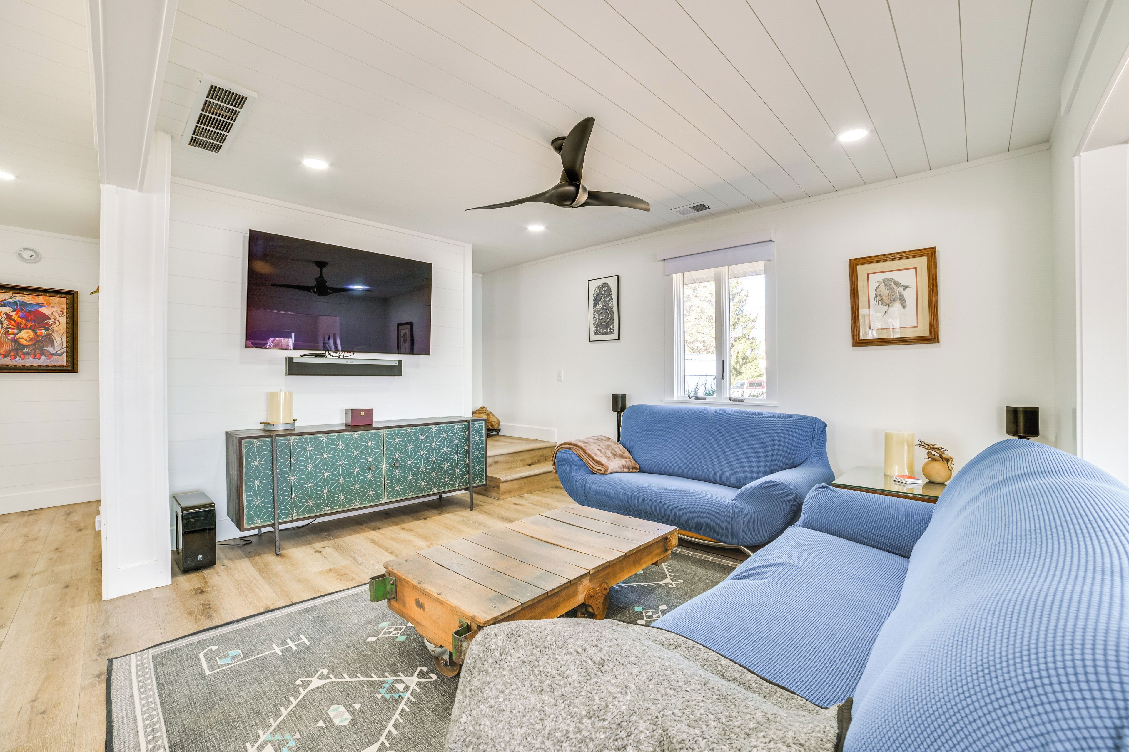 A modern living room with a blue sofa, a wooden coffee table, and a TV mounted on the wall.