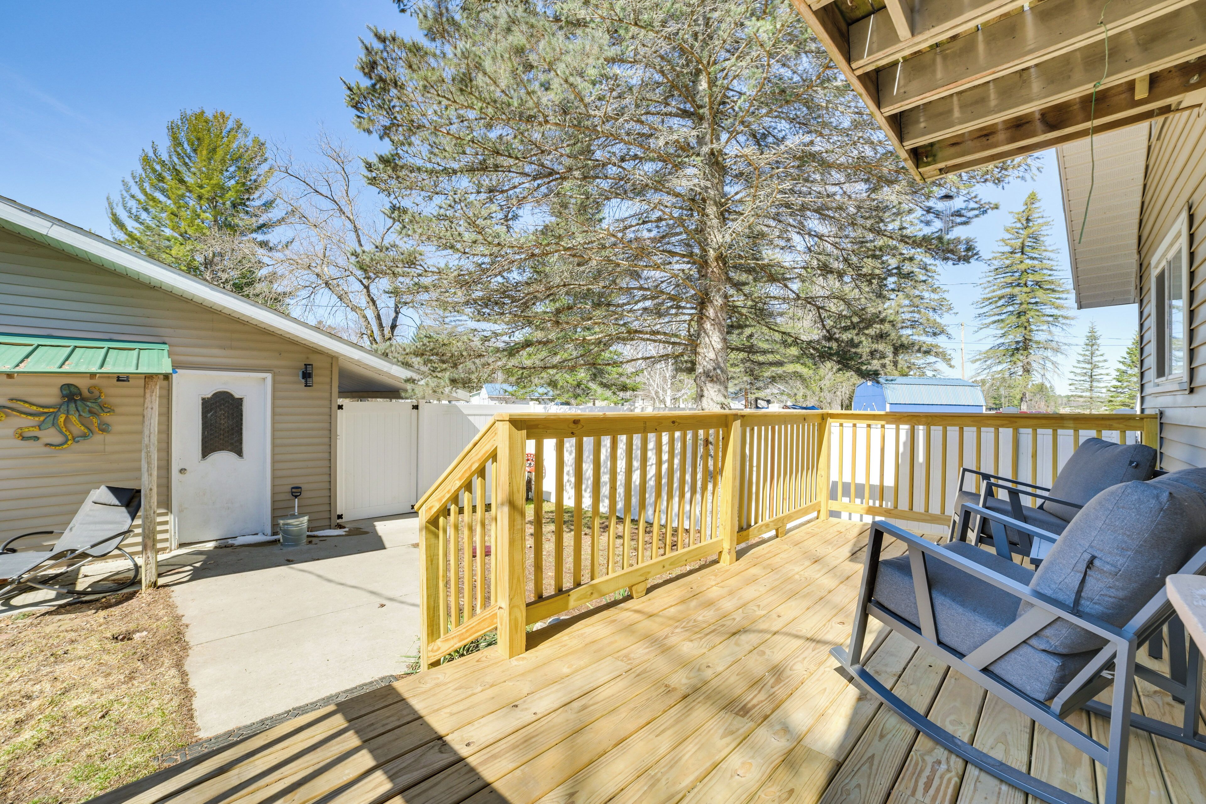 A wooden deck with outdoor furniture, a covered area, and a large tree in the background.