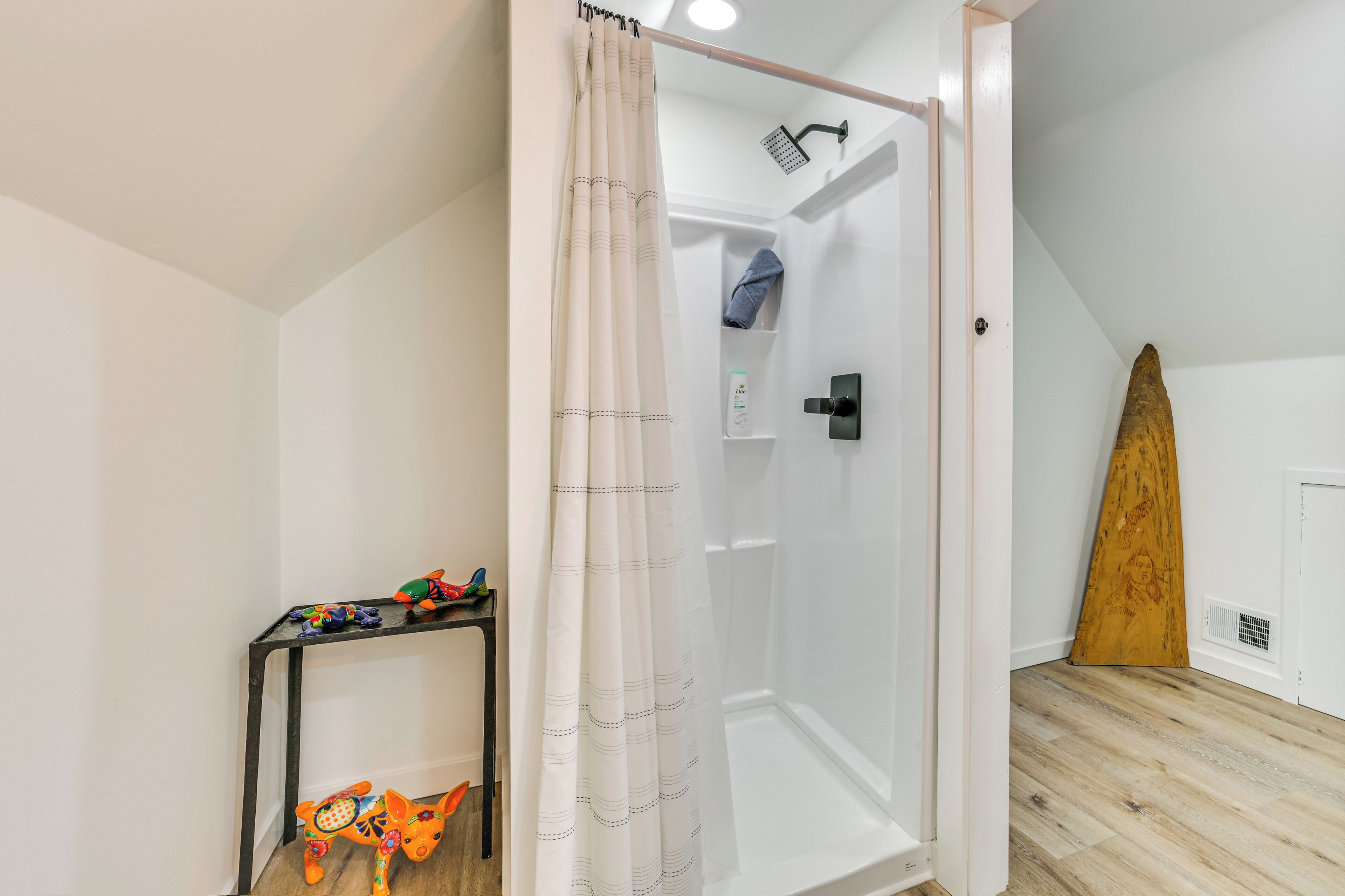 Una zona de ducha con puerta de cristal, un perchero y una tabla de surf de madera.