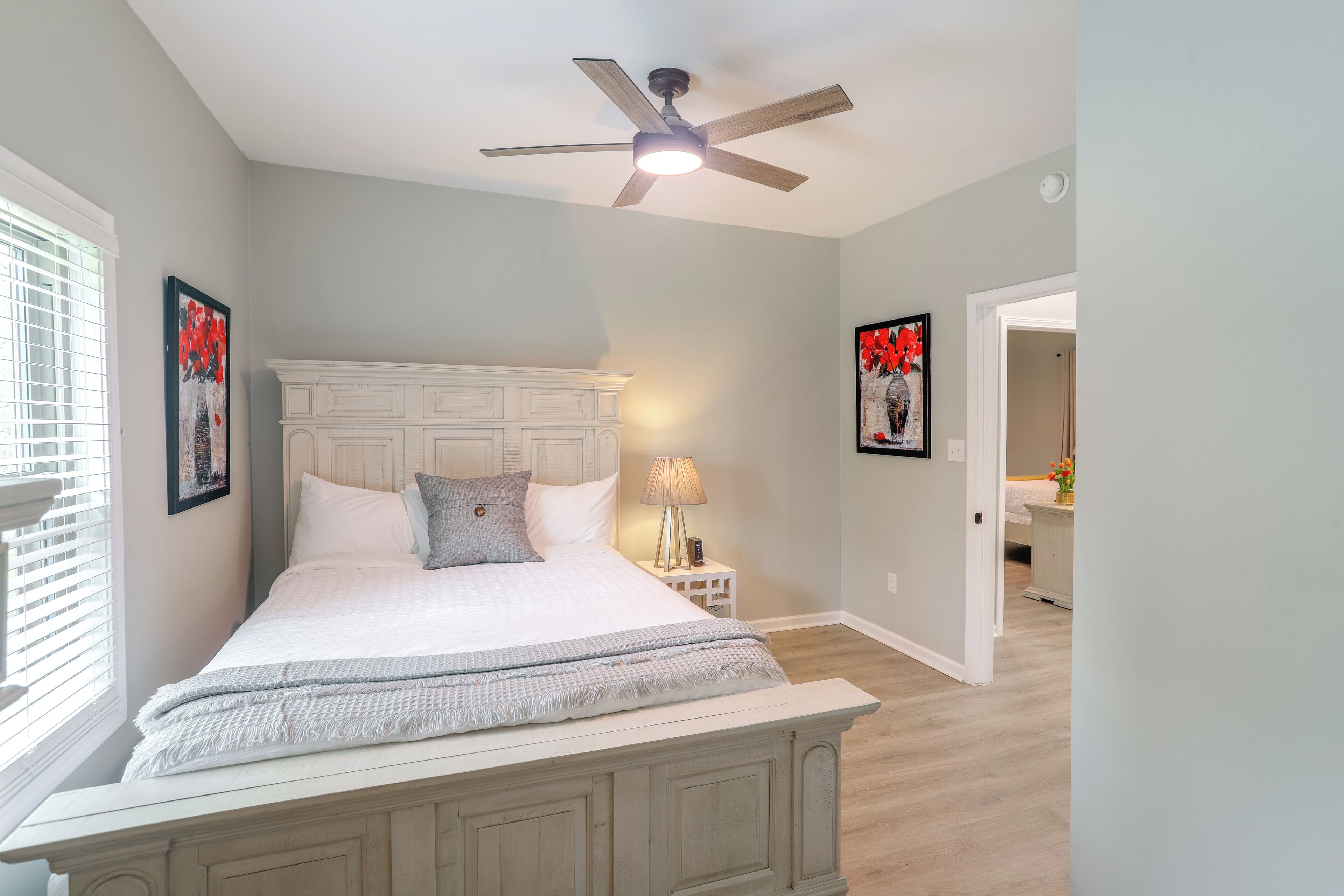 A bedroom with a large bed, a ceiling fan, and a nightstand with a lamp.