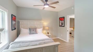 A bedroom with a large bed, a ceiling fan, and a nightstand with a lamp.