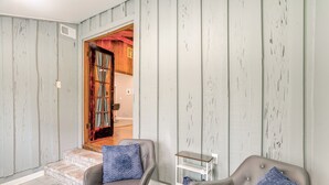 Una habitación con un sillón tapizado gris, una pequeña mesita de noche blanca y una alfombra estampada.