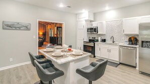 Una cocina moderna con armarios blancos, una isla central con taburetes y electrodomésticos de acero inoxidable, y vistas al área de comedor.