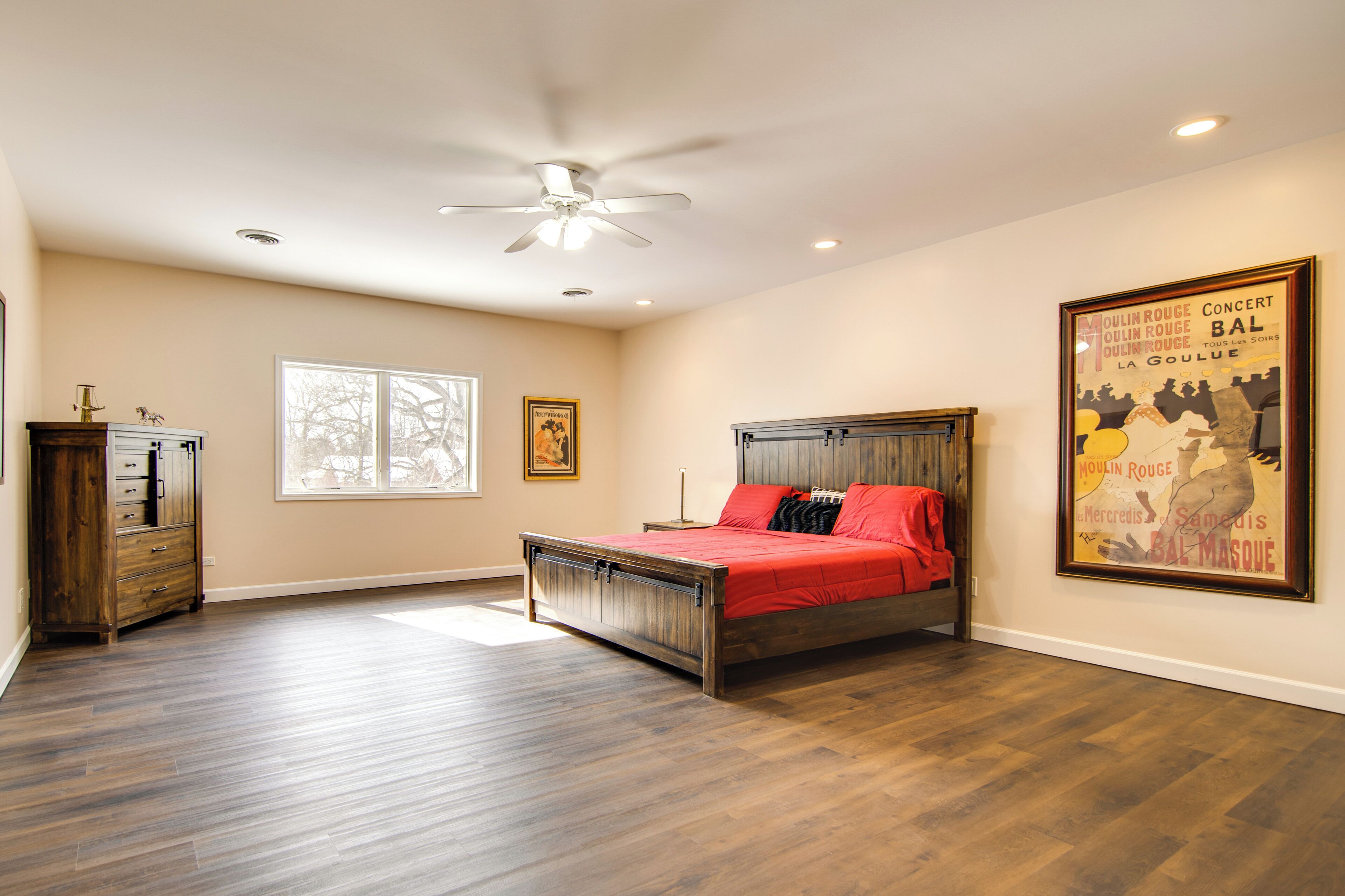 A bedroom with a bed, a ceiling fan, a window, and a poster on the wall.