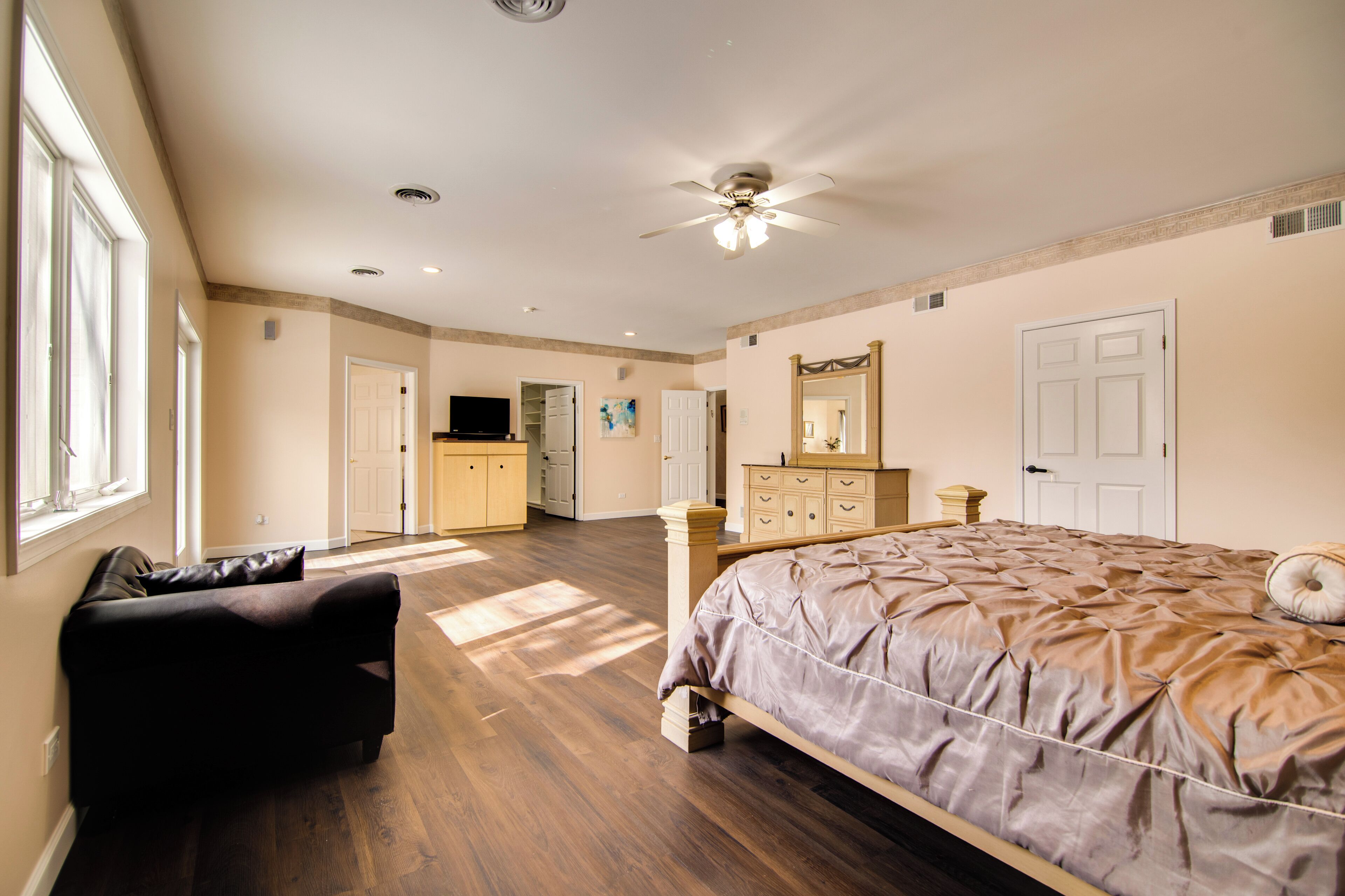 A bedroom with a bed, a dresser, a vanity, and a ceiling fan.