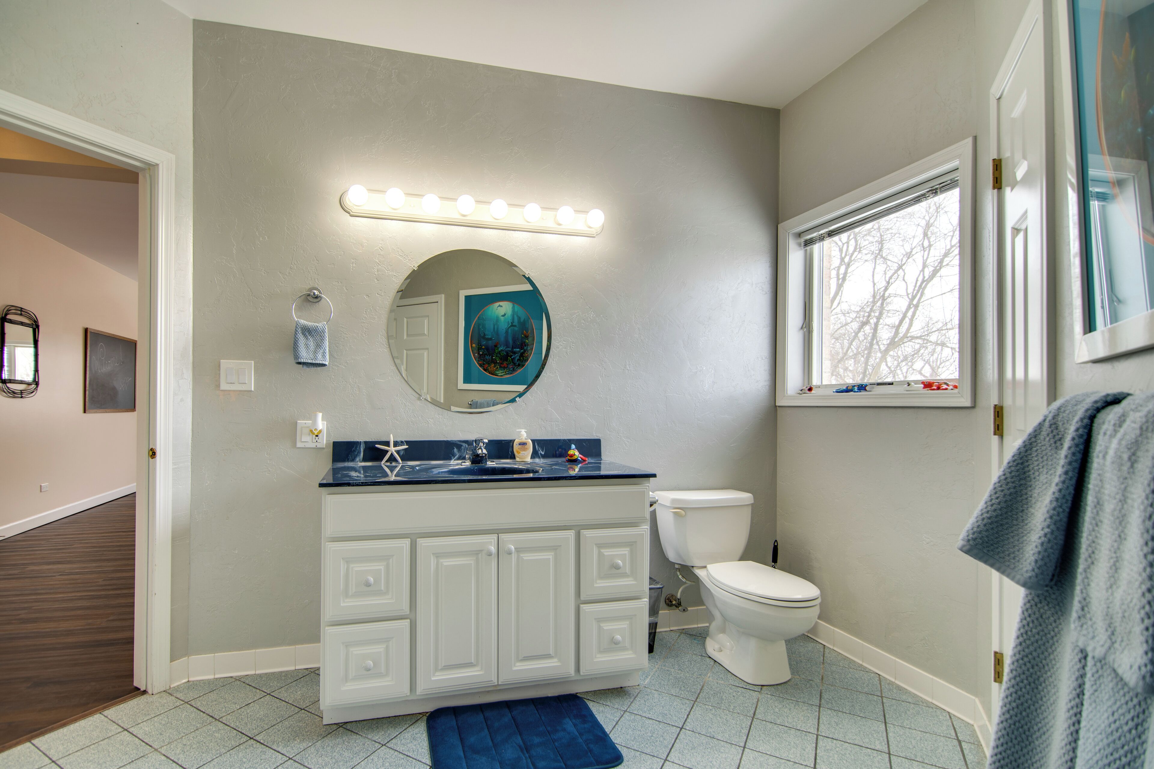 A bathroom with a white vanity, a round mirror, and a toilet.