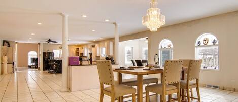 A spacious dining area with a large table and chairs, a chandelier, and a view through arched windows.