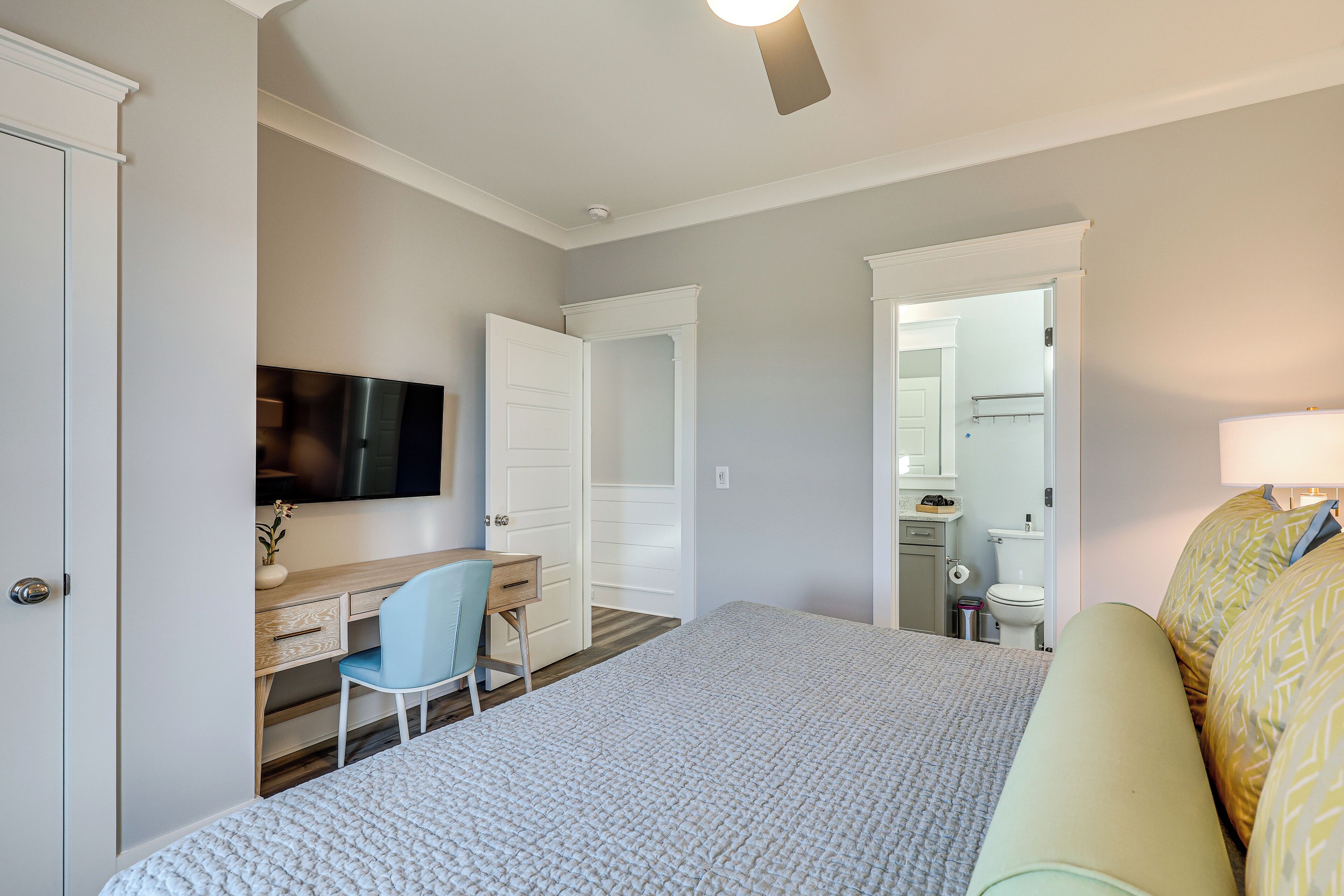 Une chambre à coucher comprenant un lit, un bureau, une chaise, un téléviseur et une salle de bain visible à travers une porte ouverte.
