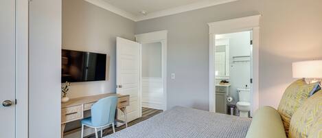 Une chambre à coucher comprenant un lit, un bureau, une chaise, un téléviseur et une salle de bain visible à travers une porte ouverte.