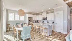 A spacious kitchen with white cabinetry, a central island, and a dining area with wicker chairs.