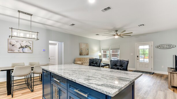 A modern kitchen with a large island, dark blue cabinets, and a marble countertop. - Walk to Beach & Harbor: Dtwn Pass Christian Home (Pass Christian)