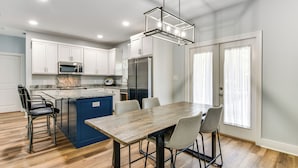 A modern kitchen with white cabinets, a blue island, and a wooden dining table with four chairs. - Walk to Beach & Harbor: Dtwn Pass Christian Home (Pass Christian)