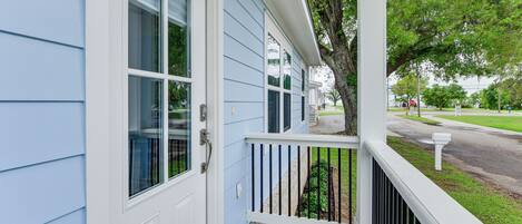 A house with a porch, a white door, and a tree in the background.
